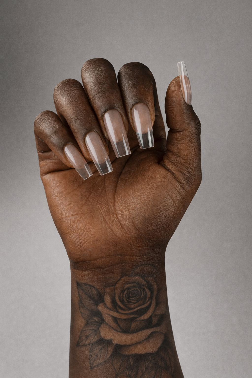 Hand with clear nail polish and a tattoo of a rose on a gray background