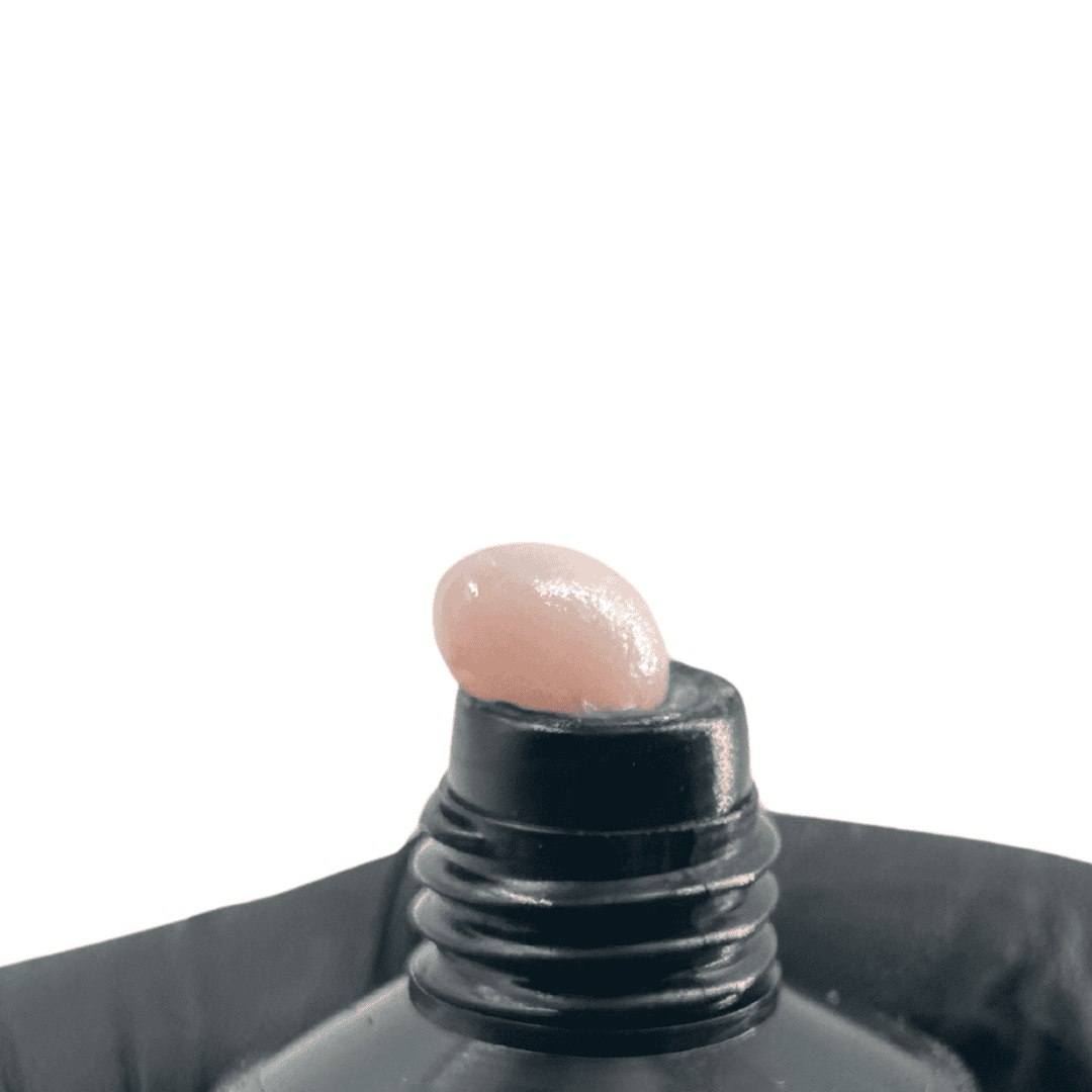 A close-up of a black tube's opening, showing a small amount of soft pink polygel protruding, indicating the color and consistency of the product for nail applications.