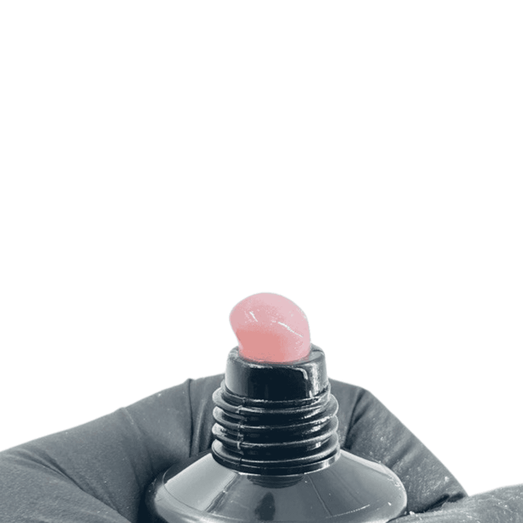 Close-up of the tube opening with a dollop of light violet-colored polygel extruding from it, held by a gloved hand against a black background.