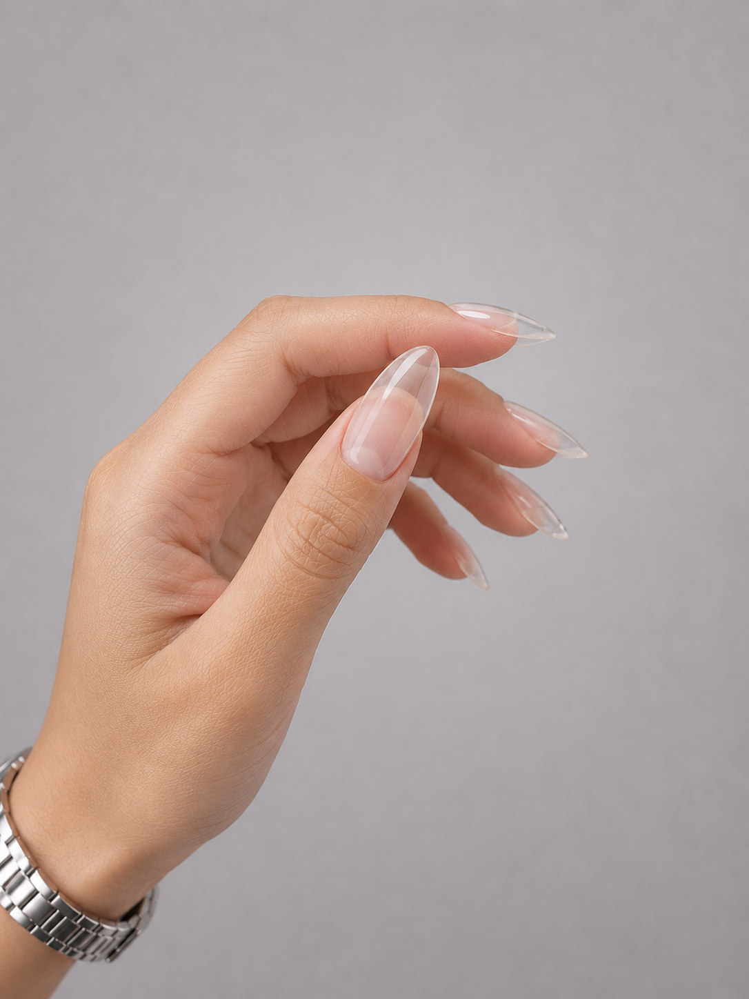 Close-up of clear almond-shaped nails created with Muse Gel Liquid PolyGel on an Asian skin tone hand. Glossy transparent nail enhancement photographed against a soft light grey background, showcasing crystal-clear clarity, smooth self-leveling application, and a natural elegant finish.