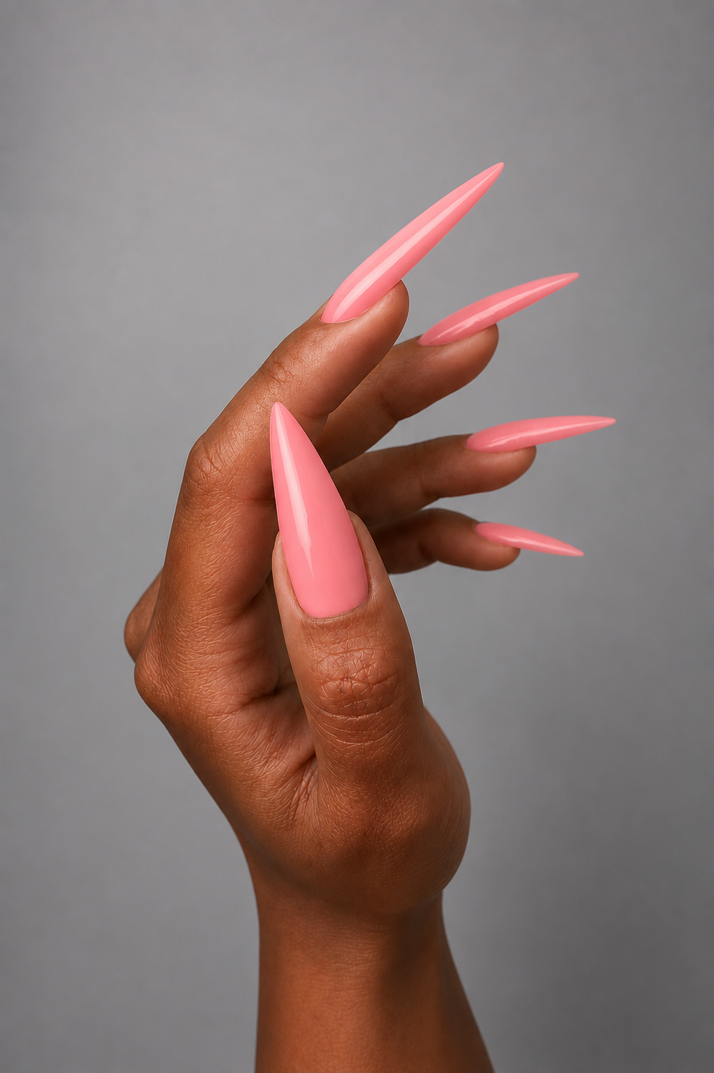 Close-up of long stiletto nails finished in a glossy coral pink gel color on a dark skin tone hand against a soft grey background. Elegant high-shine nail design showcasing smooth application and vibrant coverage by Muse Gel.